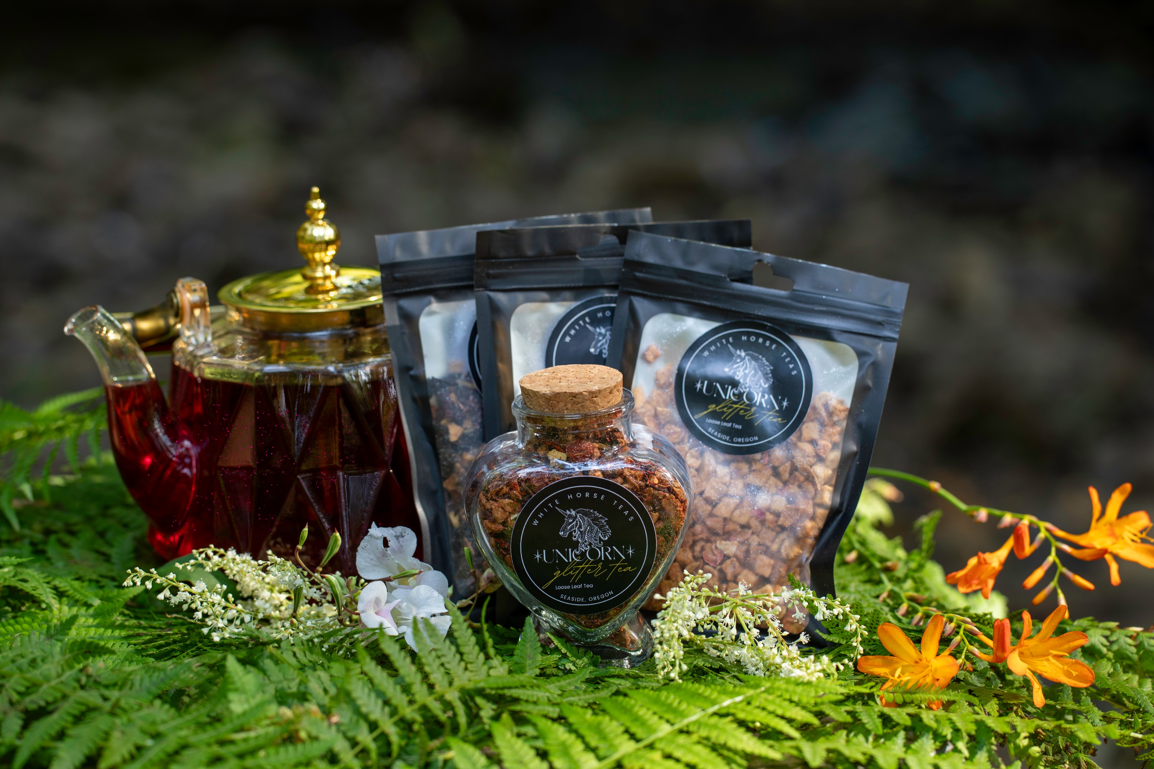 Full Unicorn Glitter Tea product lineup in ferns with orange crocosmia